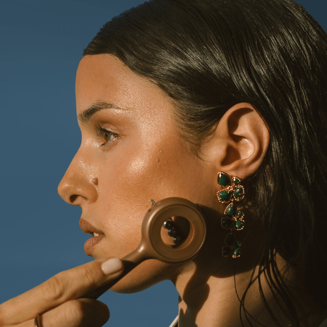 Woman using face workout depuffing sculpting tool with a blue background