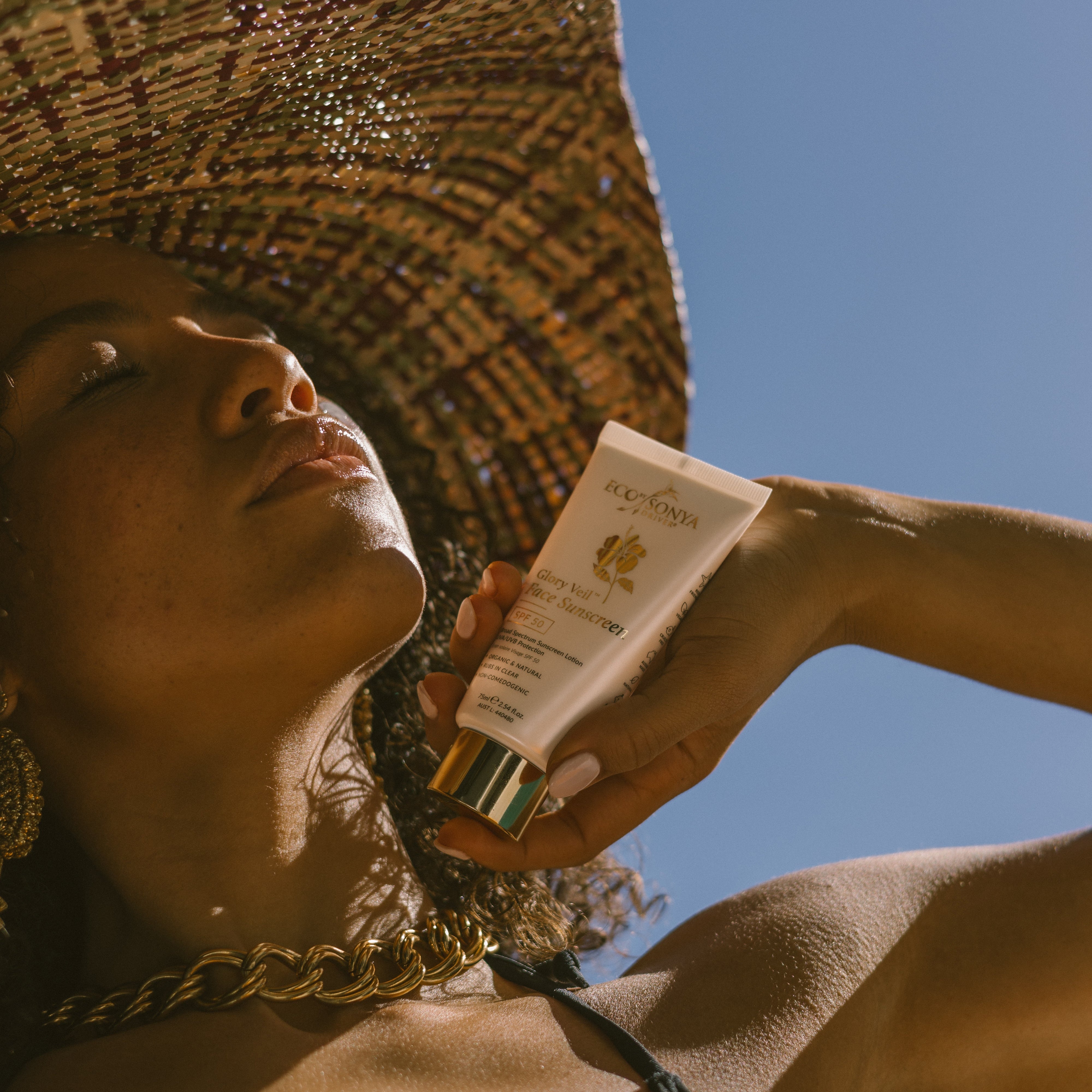 Woman showing Eco By Sonya Glory Veil Sunscreen on a blue sky background
