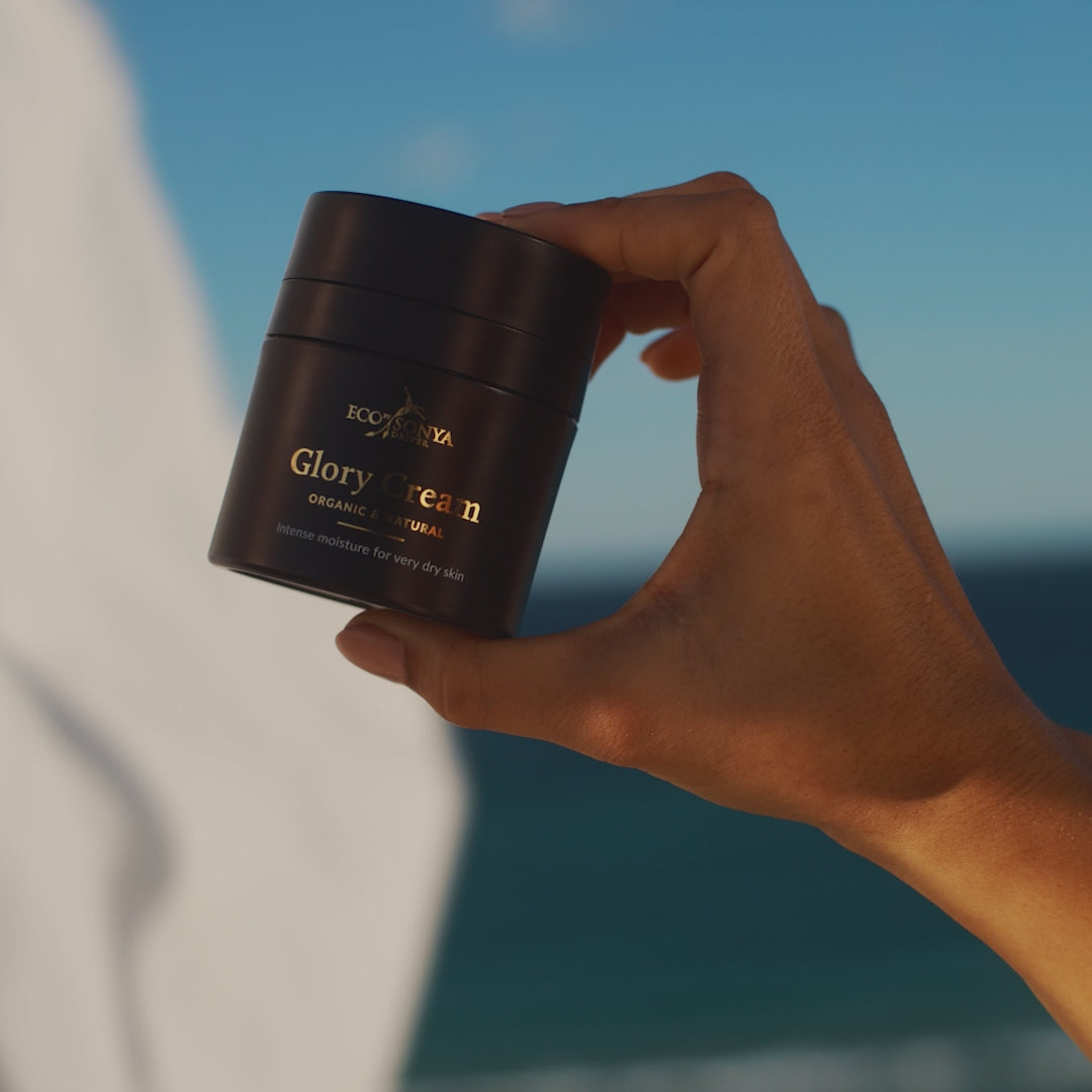 Woman applying Eco By Sonya Glory Cream rich moisturiser to her face in warm sunlight, showing smooth creamy texture and relaxed expression.